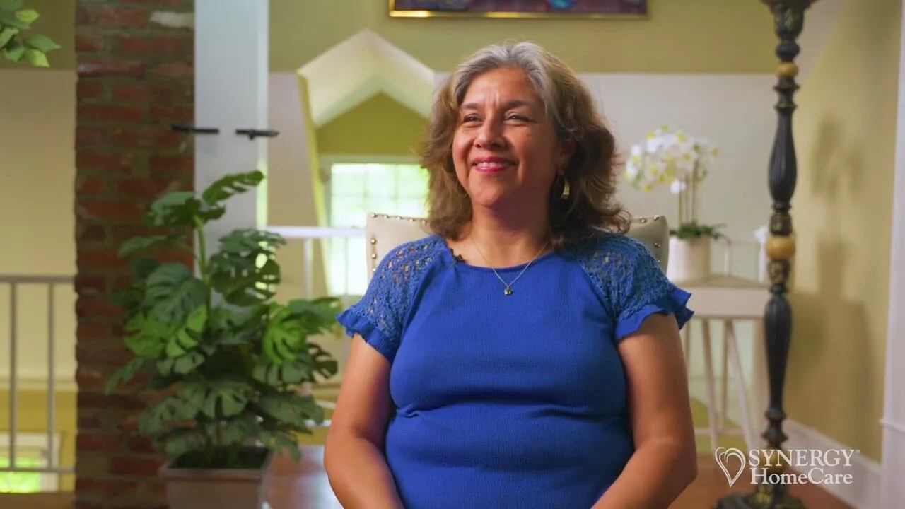 A smiling SYNERGY HomeCare client at home — play the video to meet the team