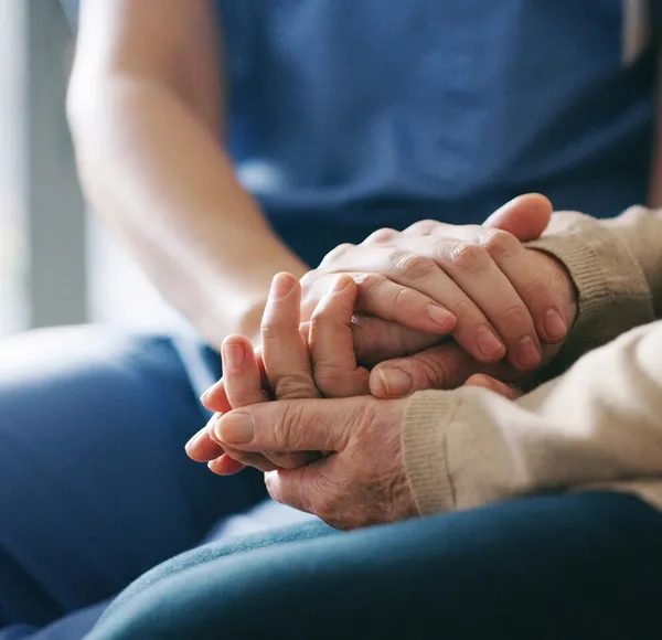 A SYNERGY HomeCare caregiver gently holding the hands of a senior client receiving cancer care