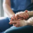 A SYNERGY HomeCare caregiver gently holding the hands of a senior client receiving cancer care