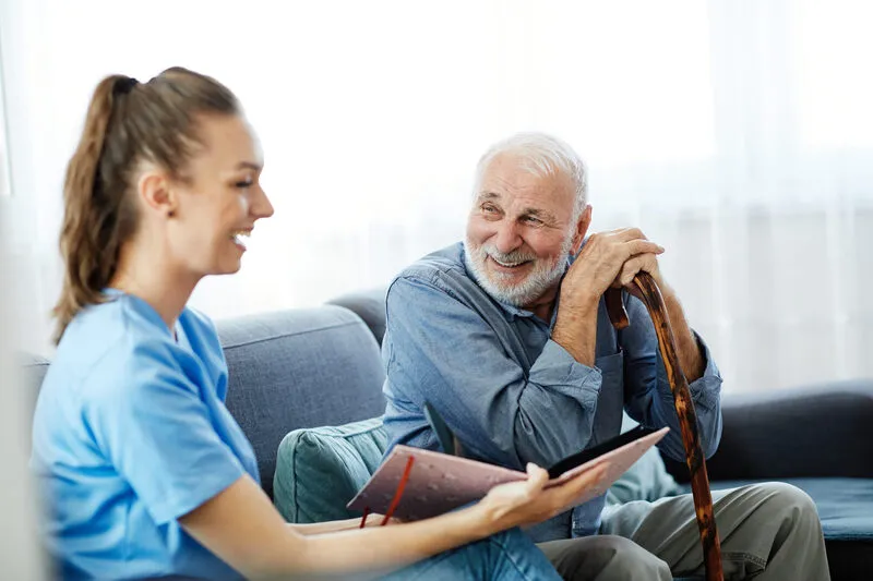 A SYNERGY HomeCare caregiver sitting with a senior man and his cane during a no-obligation in-home safety assessment