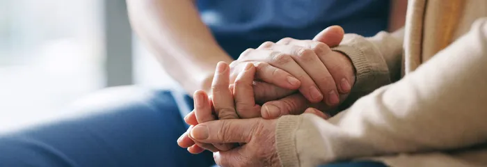 A SYNERGY HomeCare caregiver gently holding an elderly client's hands — continuous around-the-clock care