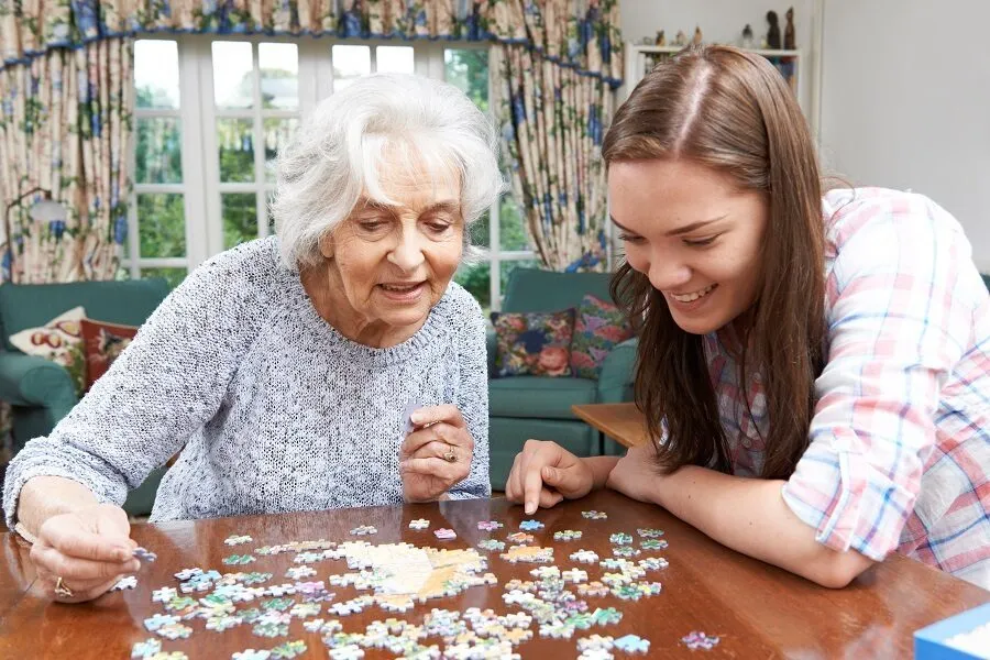 Grandmother and granddaughter working together on a jigsaw puzzle at a sunny dining room table