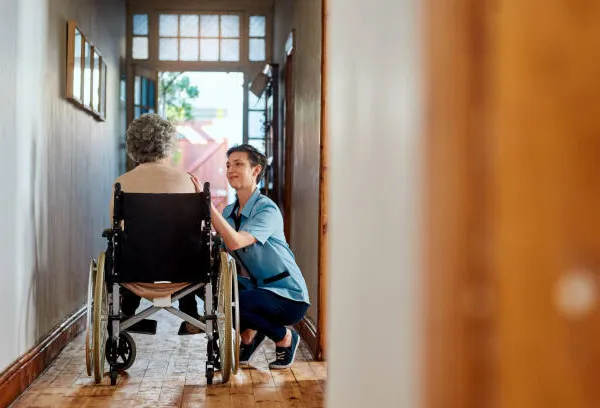 A senior man using a wheelchair at the doorway of his home, supported by in-home disability care