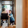 A senior man using a wheelchair at the doorway of his home, supported by in-home disability care