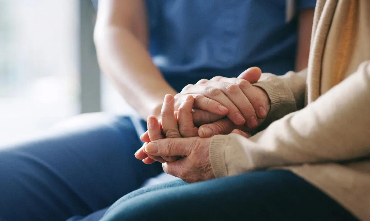 A caregiver gently holding the hands of an elderly client in reassurance