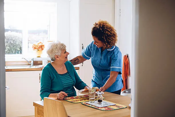 A SYNERGY HomeCare caregiver bringing a home-cooked meal to a smiling senior woman at her kitchen table