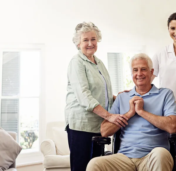 A SYNERGY HomeCare caregiver with a senior couple in a bright living room