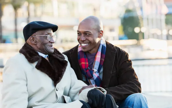 A SYNERGY HomeCare caregiver sitting and talking warmly with a smiling senior Veteran outdoors