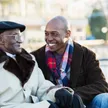 A SYNERGY HomeCare caregiver sitting and talking warmly with a smiling senior Veteran outdoors