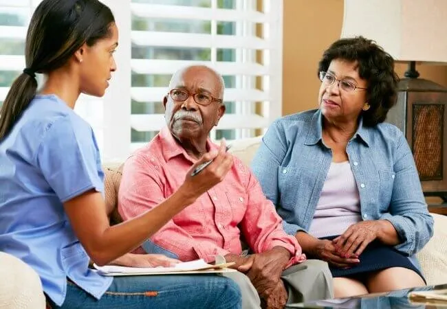 A SYNERGY HomeCare caregiver and a senior couple sharing a warm, social moment on the sofa at home